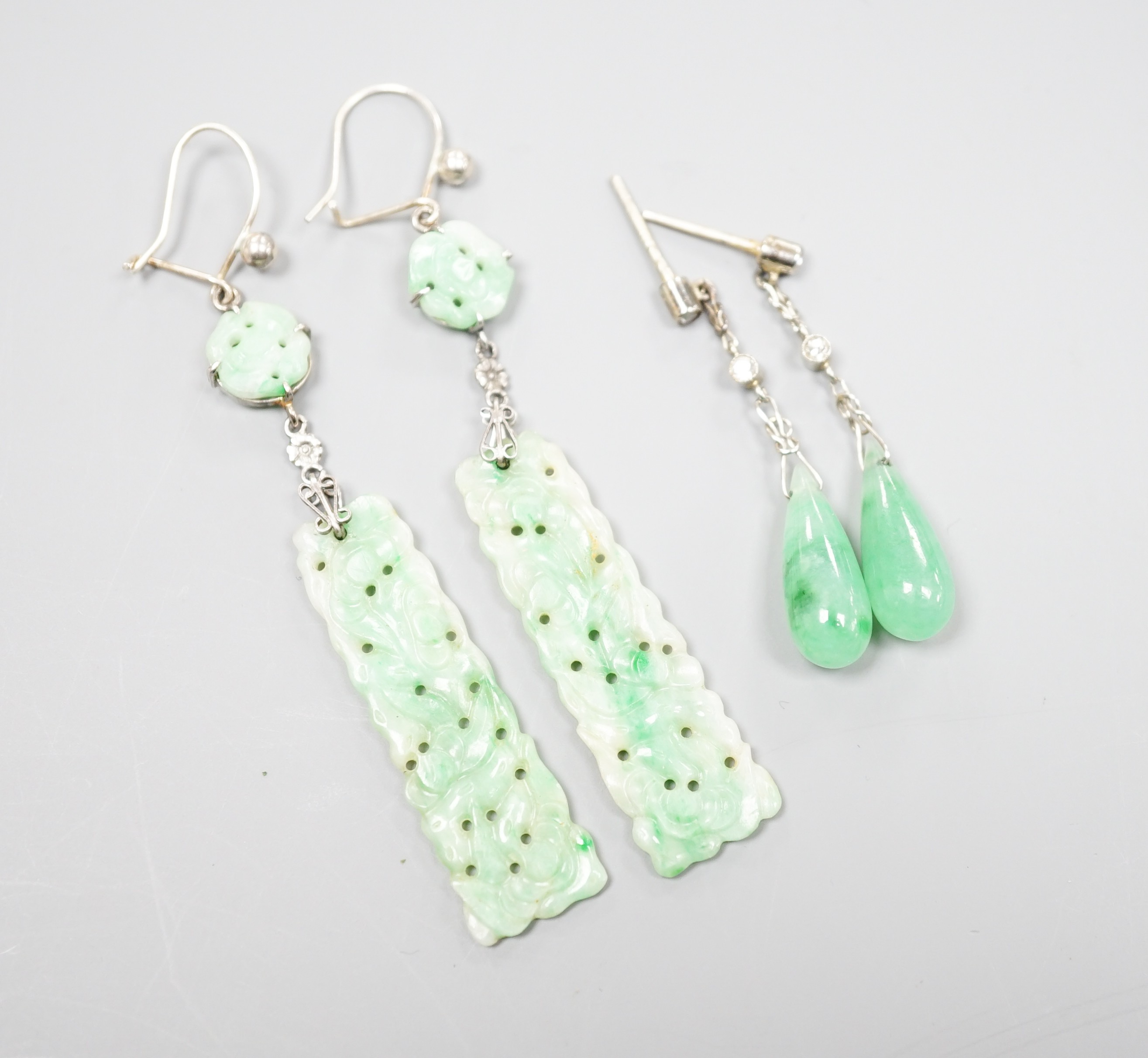 A pair of white metal pair shaped jade and two stone diamond set drop earrings, 37mm and one other pair of carved jade drop earrings, gross weight 8 grams.